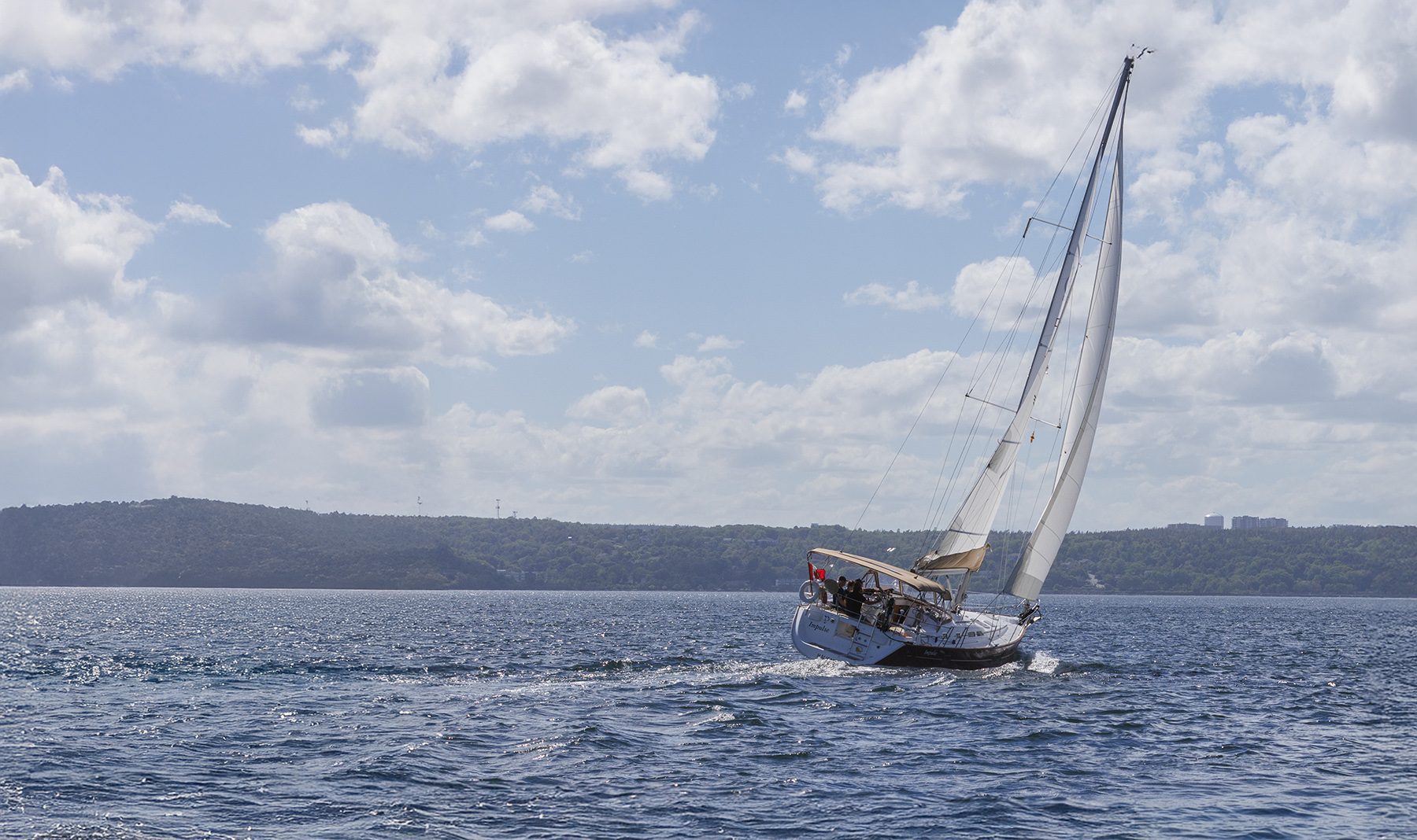 A sailboat leaning into the wind on blue water beneath a cloud-filled sky