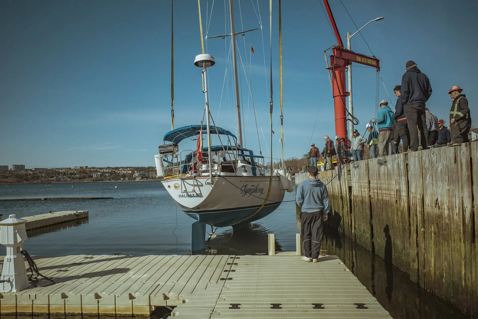 A keelboat suspended from a boatyard crane during haul-out
